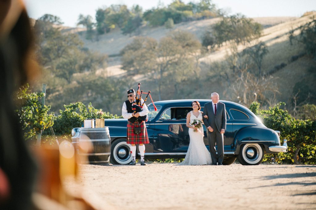 Bride exiting the old classic car while bagpipes are playing at Cass Winery Wedding by Austyn Elizabeth Photography 