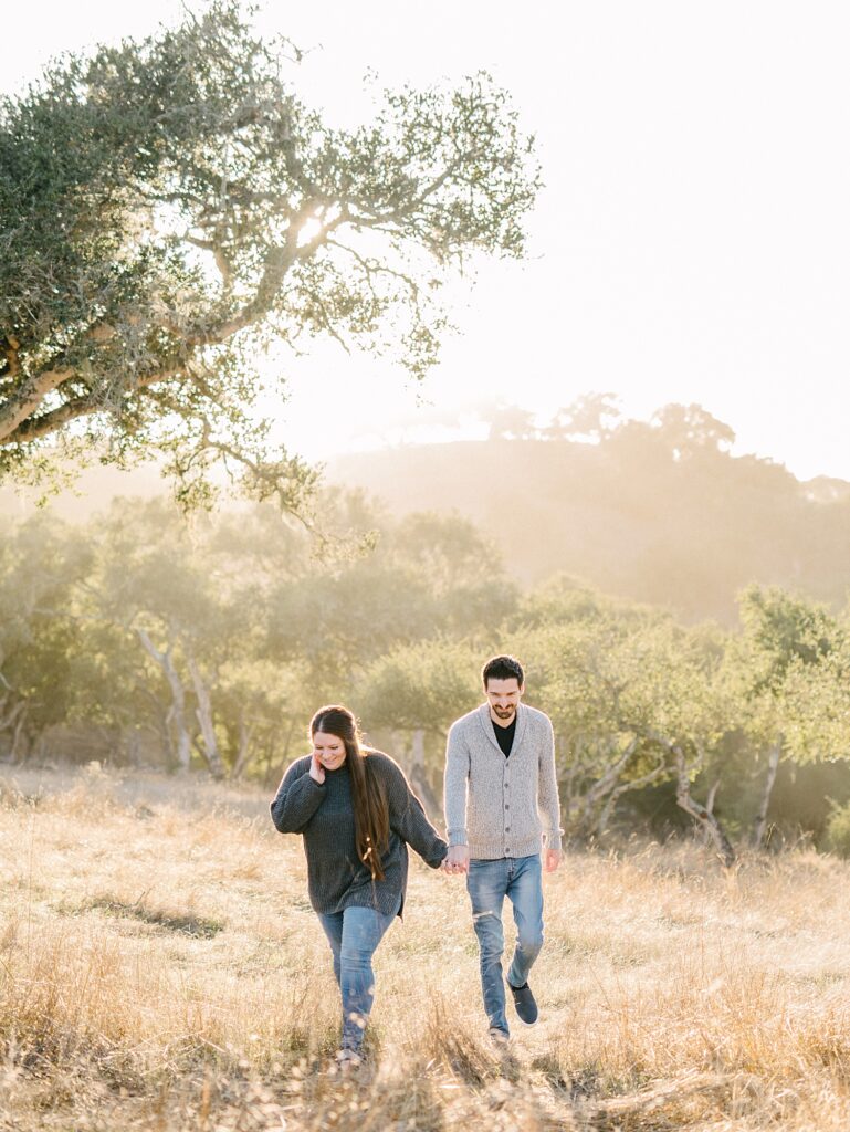 Couple walk hand in hand through golden field with rolling California hills behind for Christmas mini photo session by Arroyo Grande Wedding Photographer Austyn Elizabeth Photography