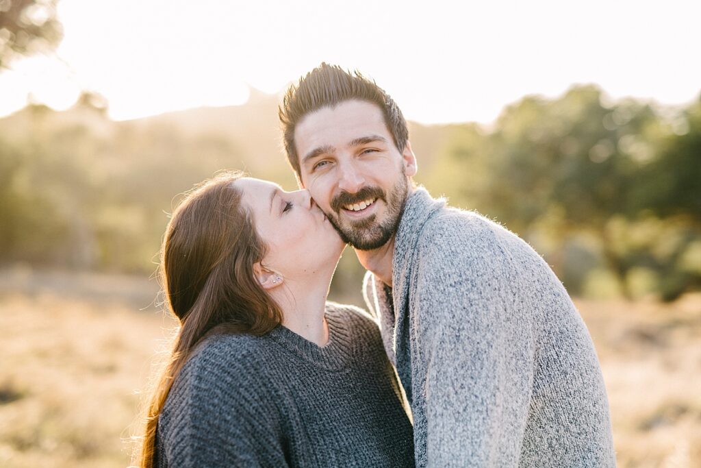 Wife kisses her husband's cheek while he smiles and the golden California light shines through for their Family Christmas Photos by Arroyo Grande Family Photographer Austyn Elizabeth Photography