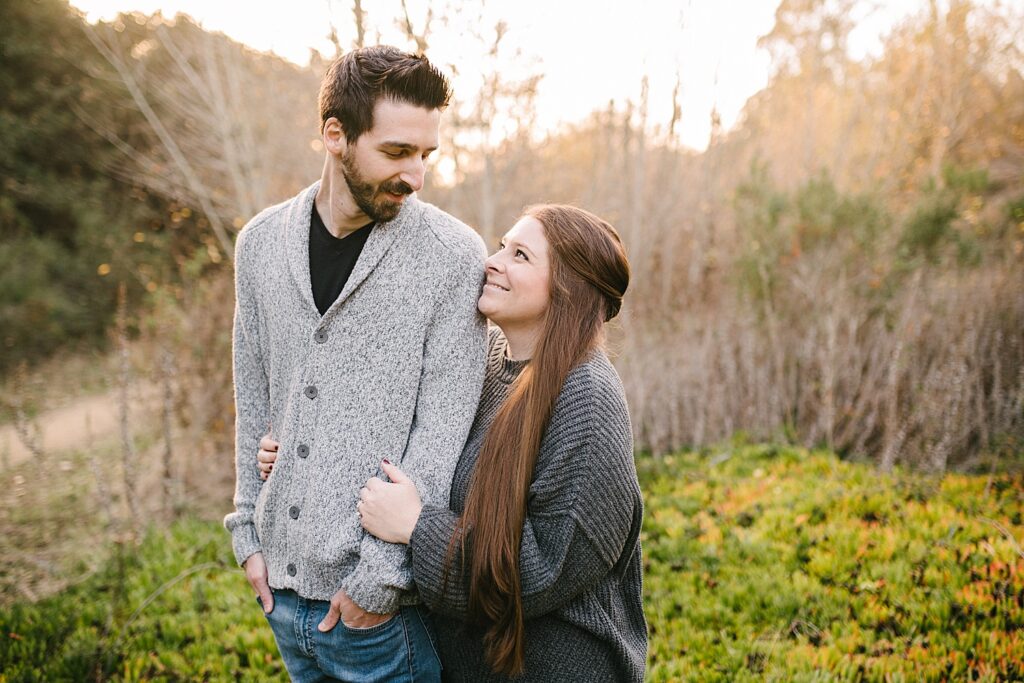 Wife stand behind husband and playfully looks up at him as he turns to look at her for Family Christmas Photos by Arroyo Grande Family Photographer Austyn Elizabeth Photography