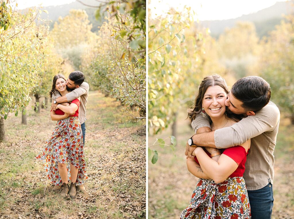Wrapping his arms around her while standing in an apple orchard at Avila Barn Engagement Session with Avila Beach Engagement Photographer Austyn Elizabeth Photography