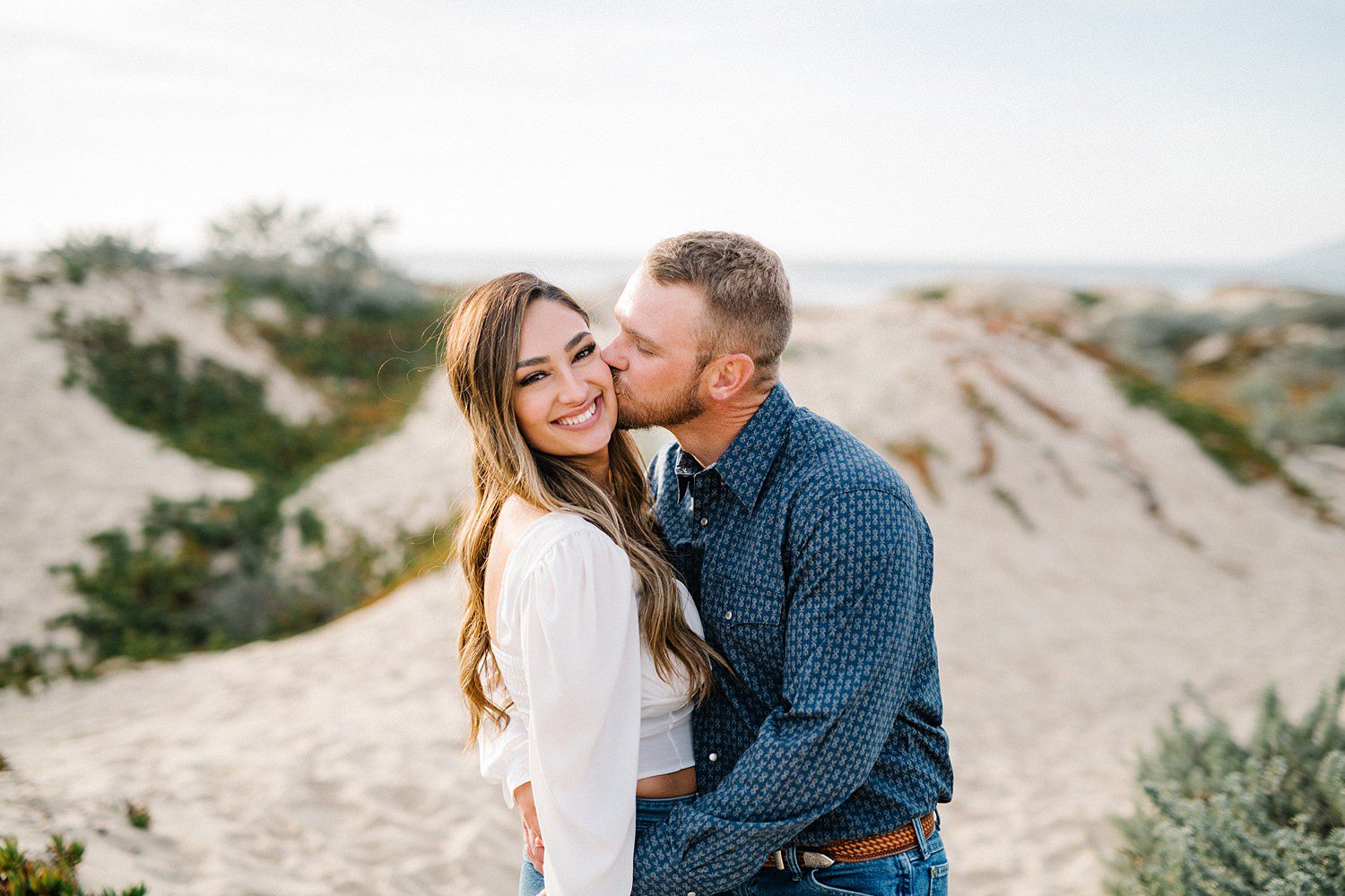 Guy kisses girl's cheek during engagement session on Pismo Beach Dunes by Pismo Beach Engagement Photographer Austyn Elizabeth Photography