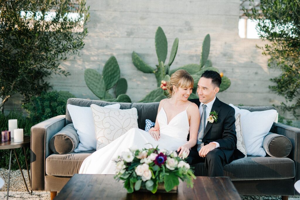 Bride and groom laughing while sitting on Avenue Twelve Rentals on specialty lounge at Biddle Ranch Vineyard Wedding by SLO Wedding Photographer Austyn Elizabeth Photography