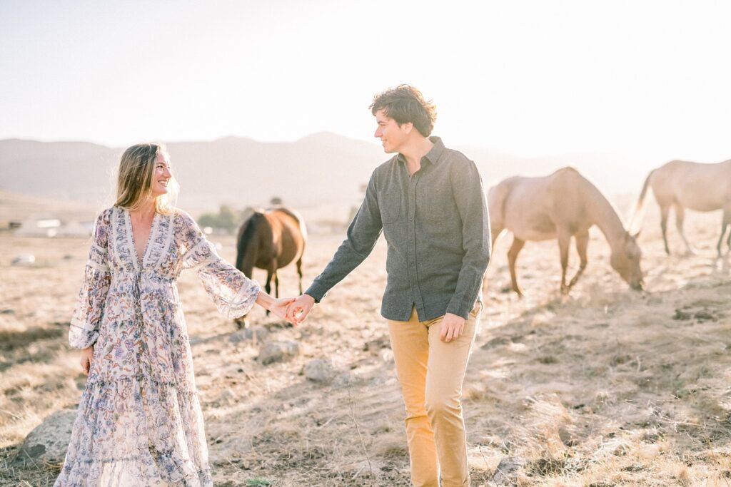 Couple walking through field with horses in the background and bride wearing anthropology dress by San Luis Obispo Wedding Photographer Austyn Elizabeth Photography