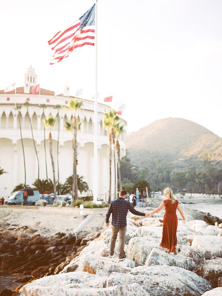 Bride and groom holding hands and walking along Avalon's breakwater towards Catalina's Casino and Descanso Bay by Catalina Wedding Photographer Austyn Elizabeth Photography 