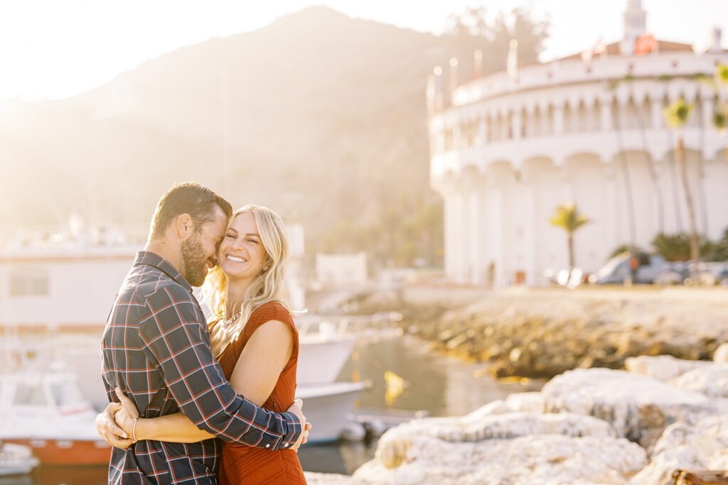 Couple embracing and bride smiling in front of Catalina's Casino by Catalina Engagement Photographer Austyn Elizabeth Photography