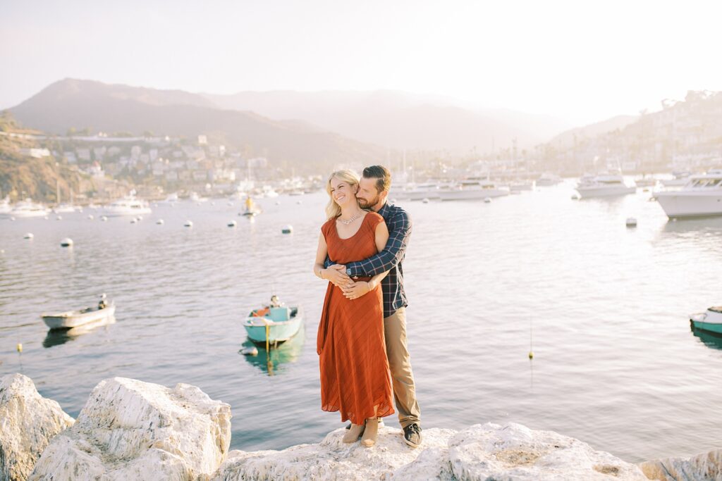 Bride and groom holding each other while standing on the breakwater with Avalon full of boats in the background by Avalon Wedding Photographer Austyn Elizabeth Photography