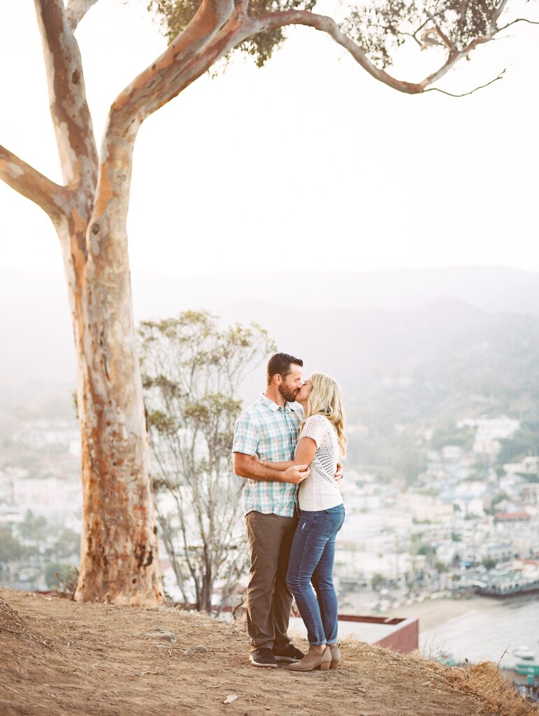 Bride and groom embracing while next to a eucalyptus tree overlooking the small town of Avalon by Catalina Engagement Photographer Austyn Elizabeth Photography