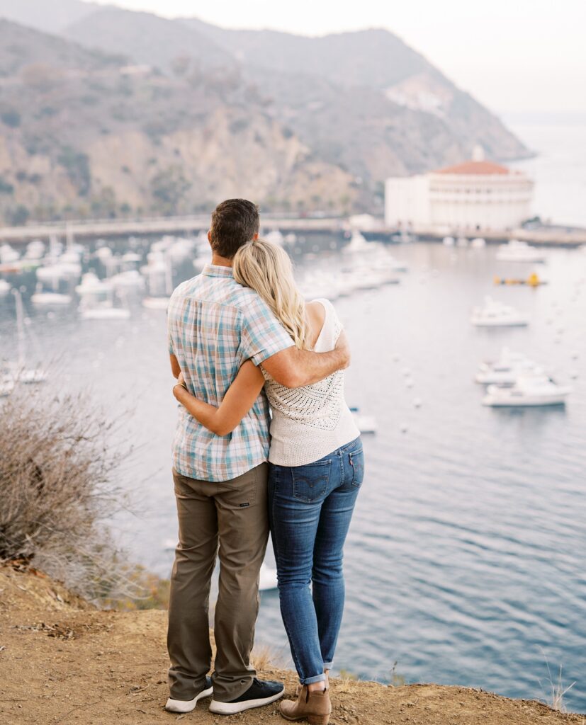 Couple hold each other close as they view Catalina's iconic Casino in the background by Avalon Engagement Photographer Austyn Elizabeth Photography