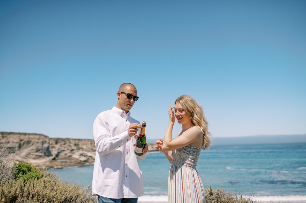 Opening a bottle of bubbly at surprise proposal at Montana De Oro's Spooners Cove by Pismo beach engagement photographer austyn elizabeth photography