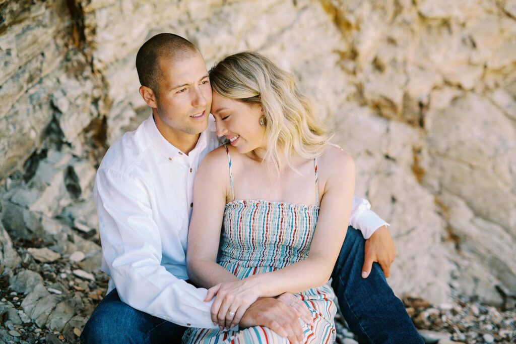 girl snuggles up to fiance while sitting looking at the ocean at surprise proposal at Montana De Oro's Spooners Cove by Pismo beach engagement photographer austyn elizabeth photography