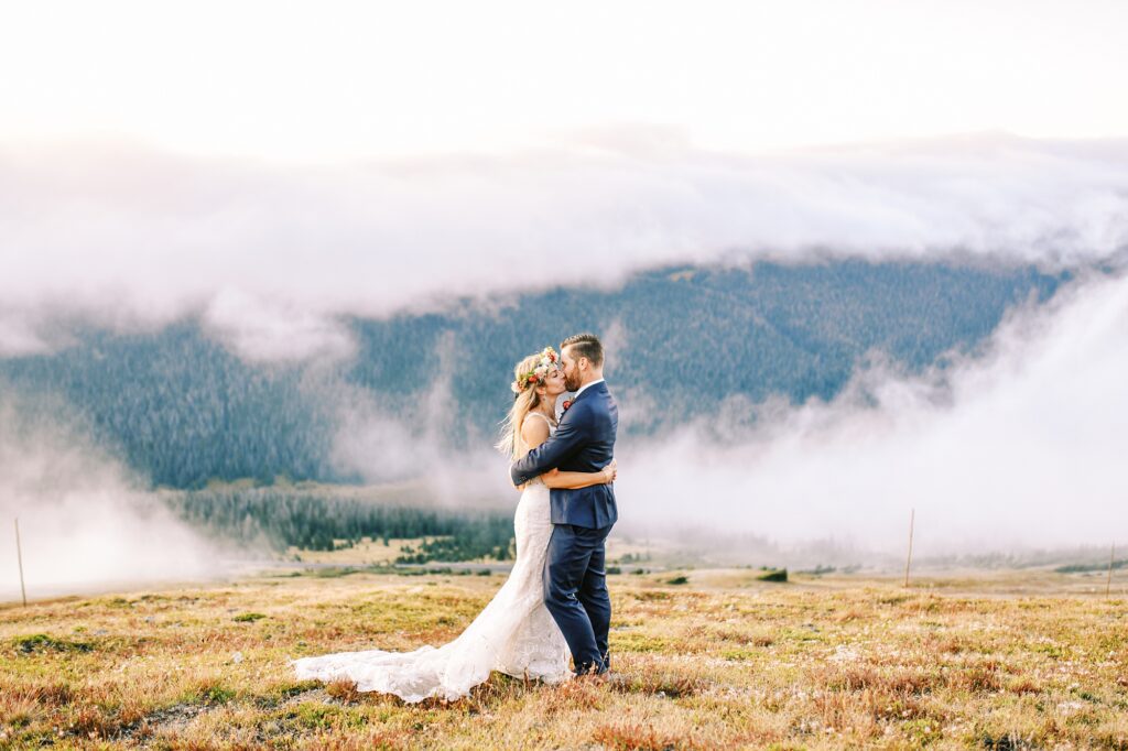 on top of trail ridge road with bride and groom kissing as clouds part at Destination Rocky Mountain National Forest Wedding by Estes park Wedding Photographer Austyn Elizabeth Photography