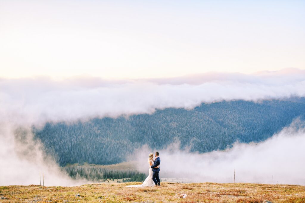 on top of trail ridge road with bride and groom holding each other as clouds part at Destination Rocky Mountain National Forest Wedding by Estes park Wedding Photographer Austyn Elizabeth Photography