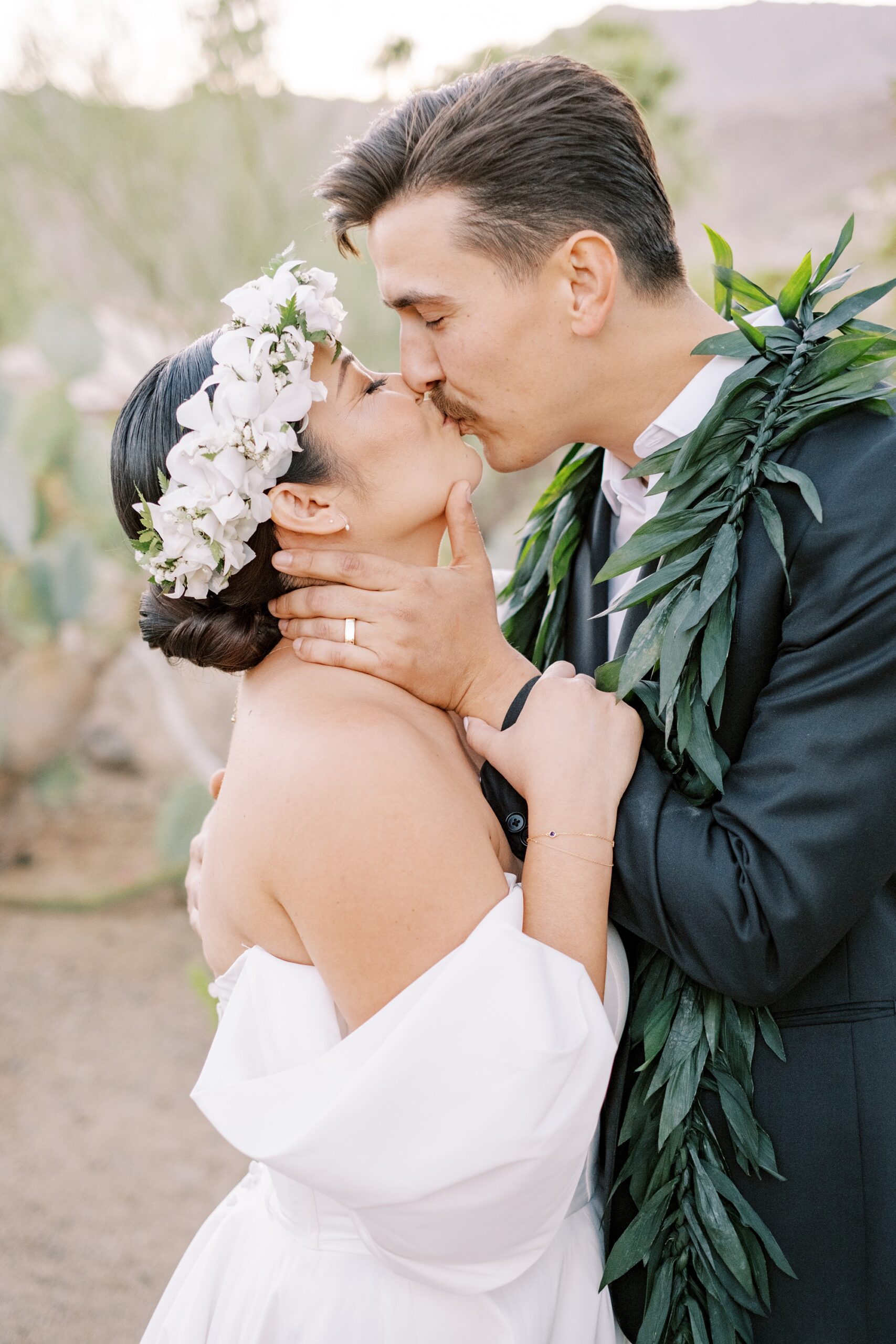 Bride in white floral crown kissing husband wearing hawaiian lei at Villa Leche wedding by Palm Springs Wedding Photographer Austyn Elizabeth Photography