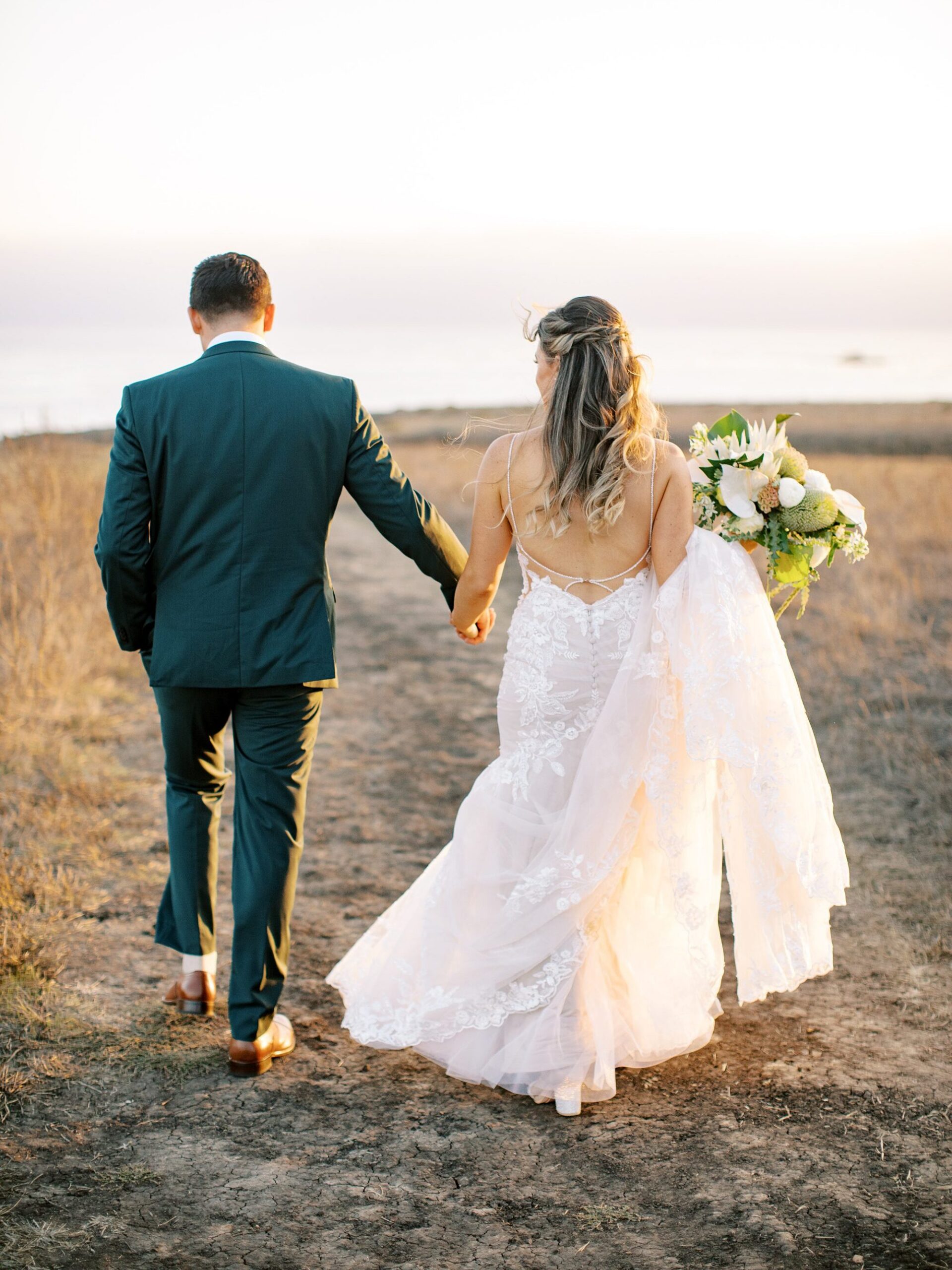 Couple walk away hand in hand by Cayucos open field by Cayucos Wedding Photographer on Film by Austyn Elizabeth Photography