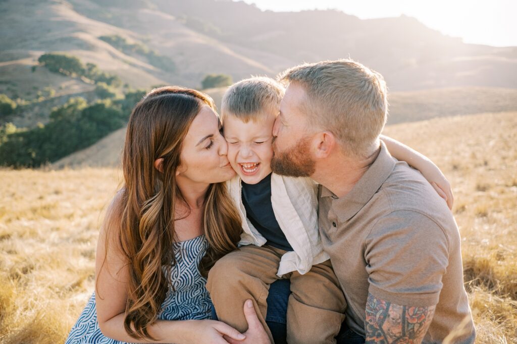 Mom and Dad kiss squeeze their kids face during San Luis Obispo family photos at Johnson Ranch Trail by Pismo Beach Family Photographer Austyn Elizabeth Photography