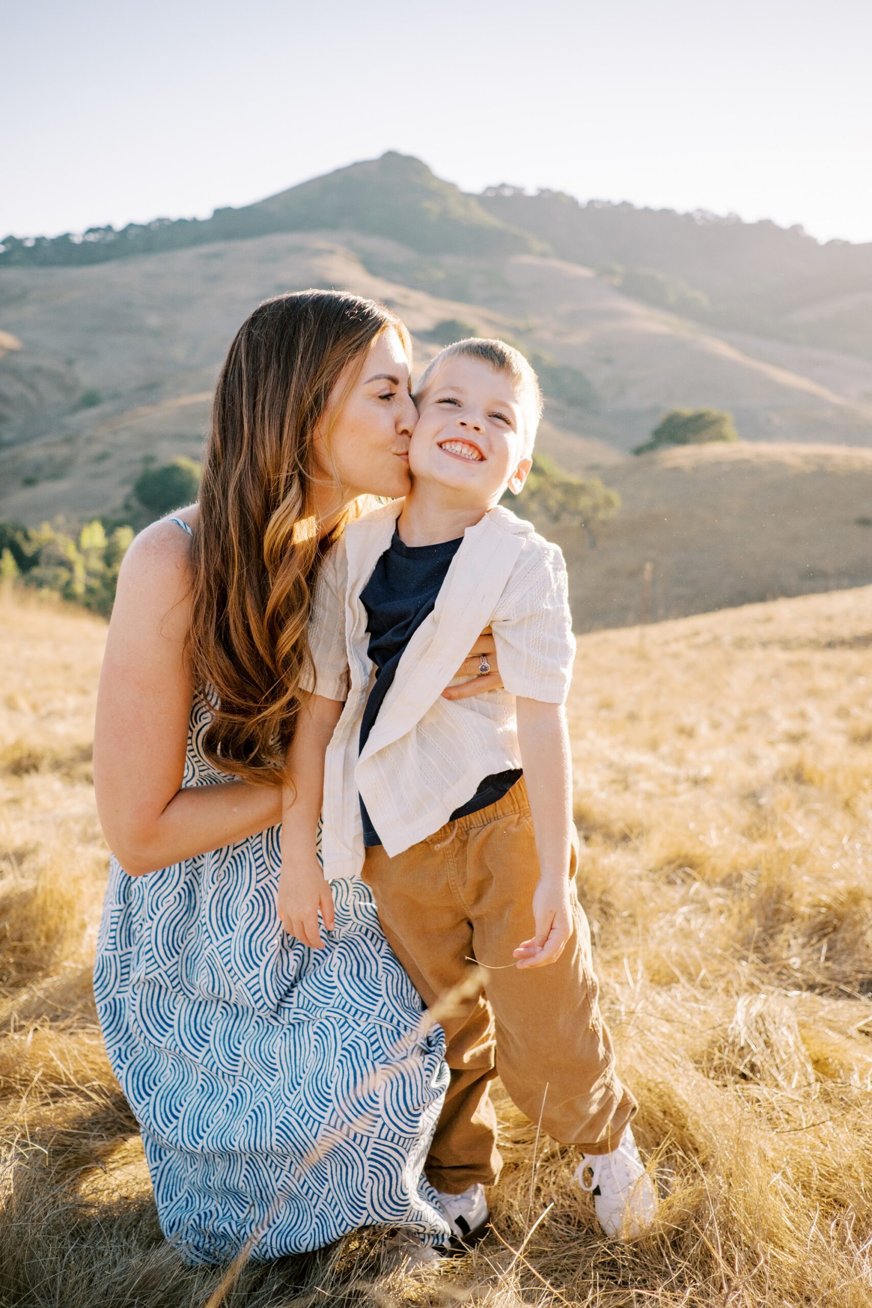 Mom kisses little boy with big teethy grin at Johnson Ranch Trail by Pismo Beach Family Photographer Austyn Elizabeth Photography