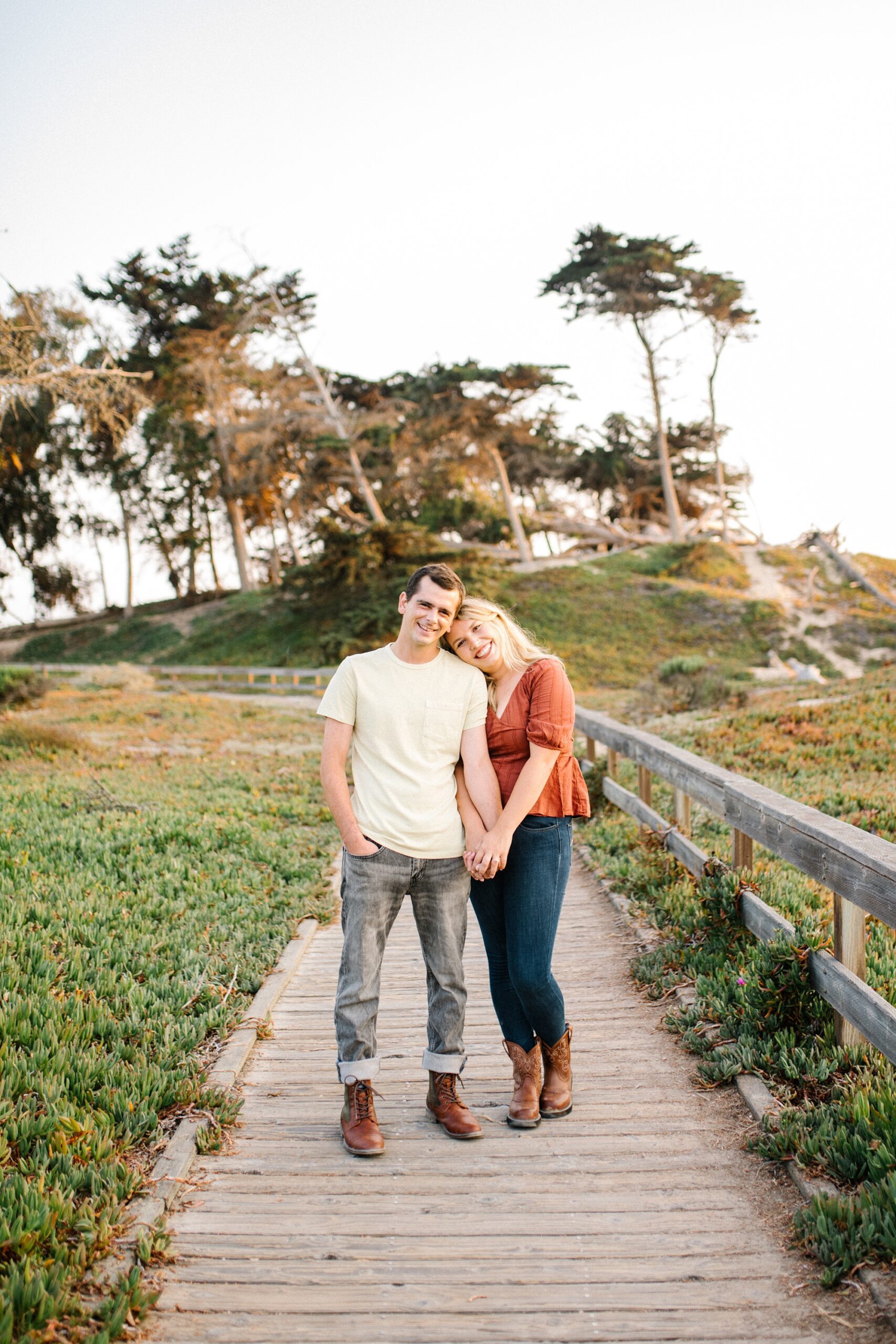 Couple smiles while standing on Pismo beach board walk by Pismo Beach Engagement Photographer Austyn Elizabeth Photography