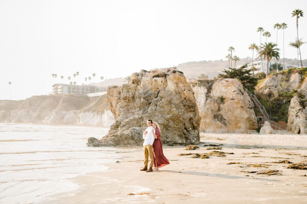 Couple stand in front of large rock during Pismo beach engagement session by Pismo Beach Engagement Photographer Austyn Elizabeth Photography
