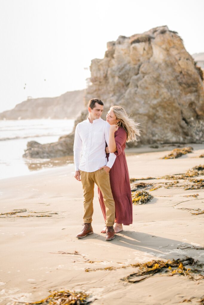 Engaged couple stand on the beach by Pismo Beach Engagement Photographer Austyn Elizabeth Photography