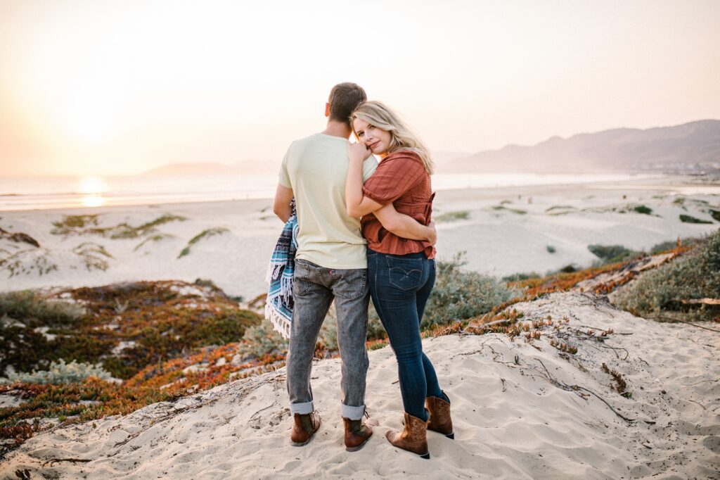 Standing on sand dune with sunset over the ocean by Pismo Beach Engagement Photographer Austyn Elizabeth Photography