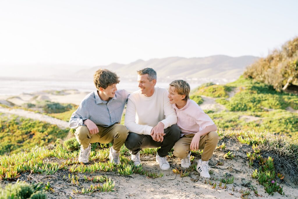 Dad and his two teen boys squat on pismo dunes by Pismo Beach Family Photographer Austyn Elizabeth Photography