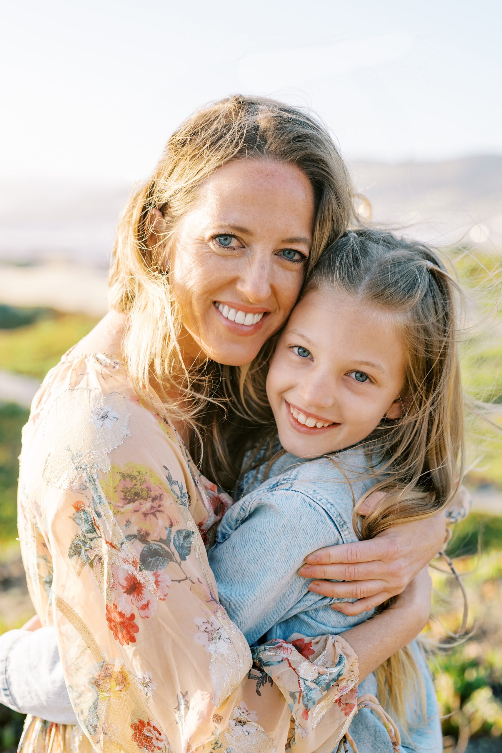 Mom and daughter with blue eyes hug each other with pismo beach in the background by Pismo Beach Family Photographer Austyn Elizabeth Photography