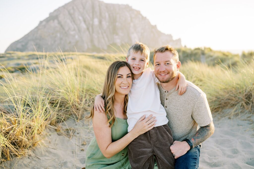 Family looking at the camera with beach grass and morro rock in the back ground by Morro Bay Family Photographer Austyn Elizabeth Photography