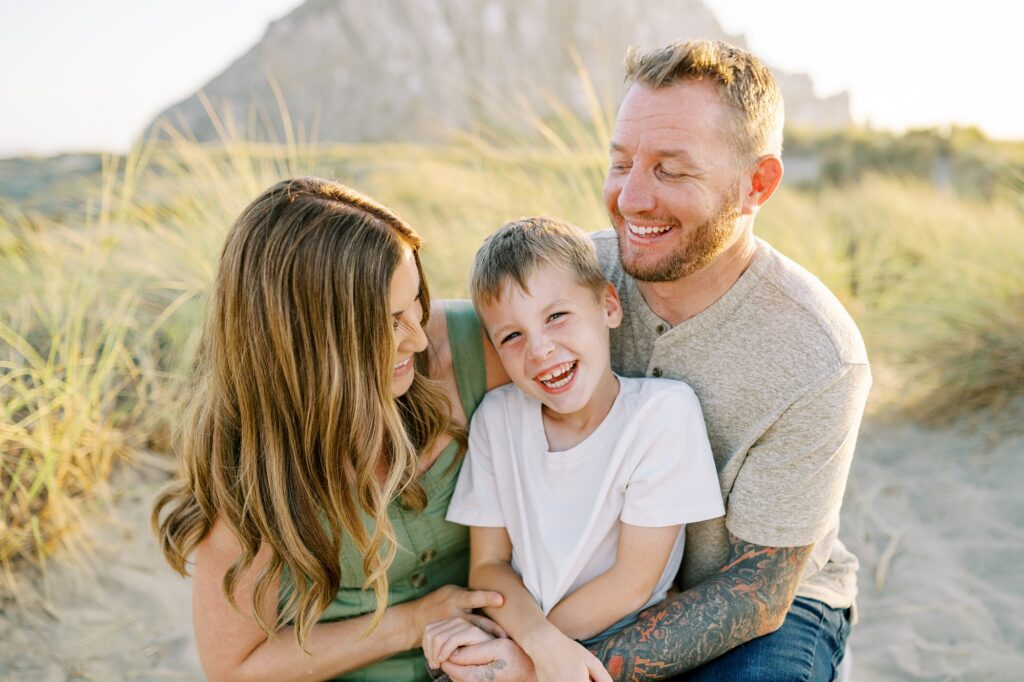 Parents looking and tickling their 8 year old during Morro Bay Family Photos in front of Morro Rock by Pismo Beach Family Photographer Austyn Elizabeth Photography