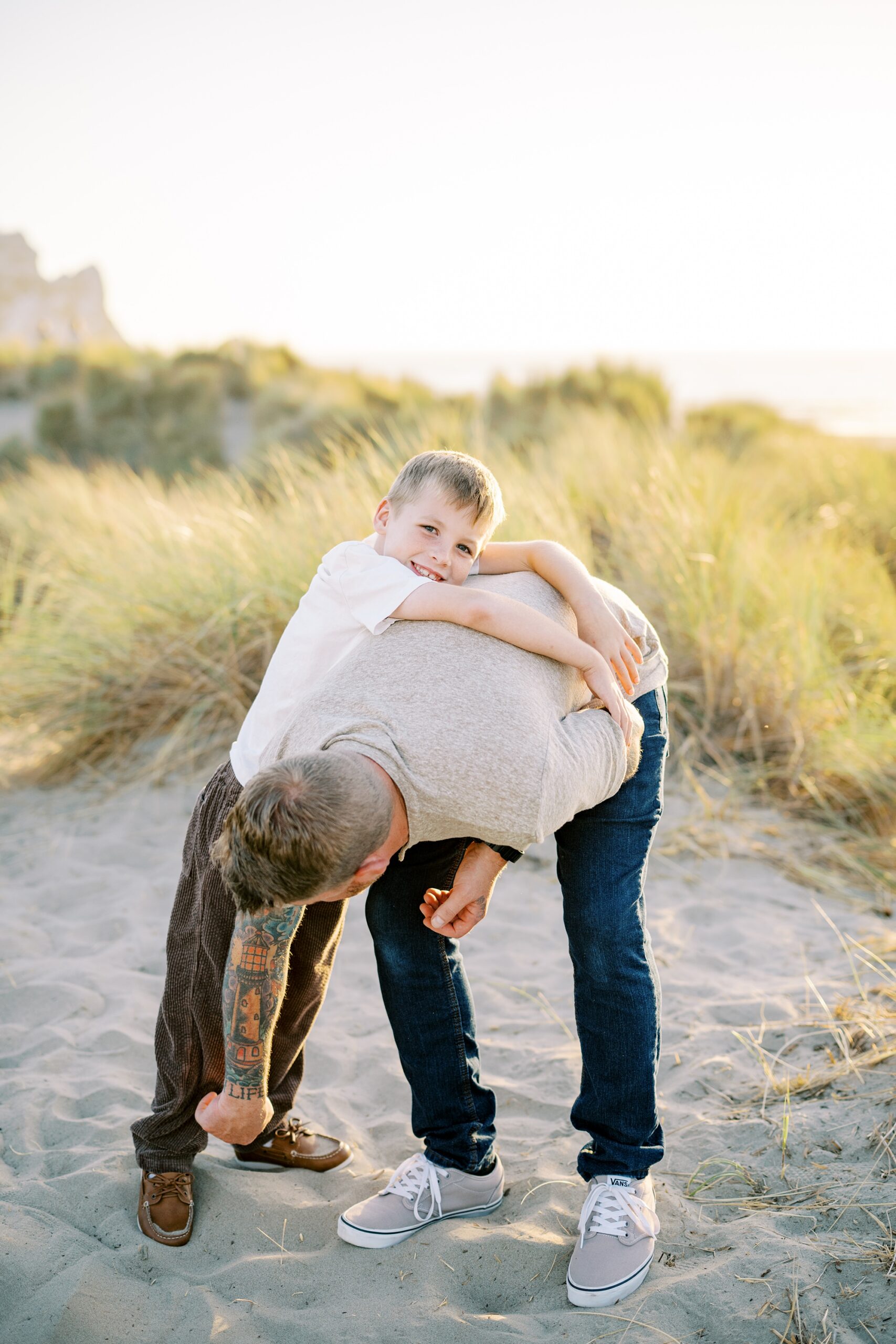 eight year old crawling onto dad's back during their morro rock family photos by Morro Bay Family Photographer Austyn Elizabeth Photography