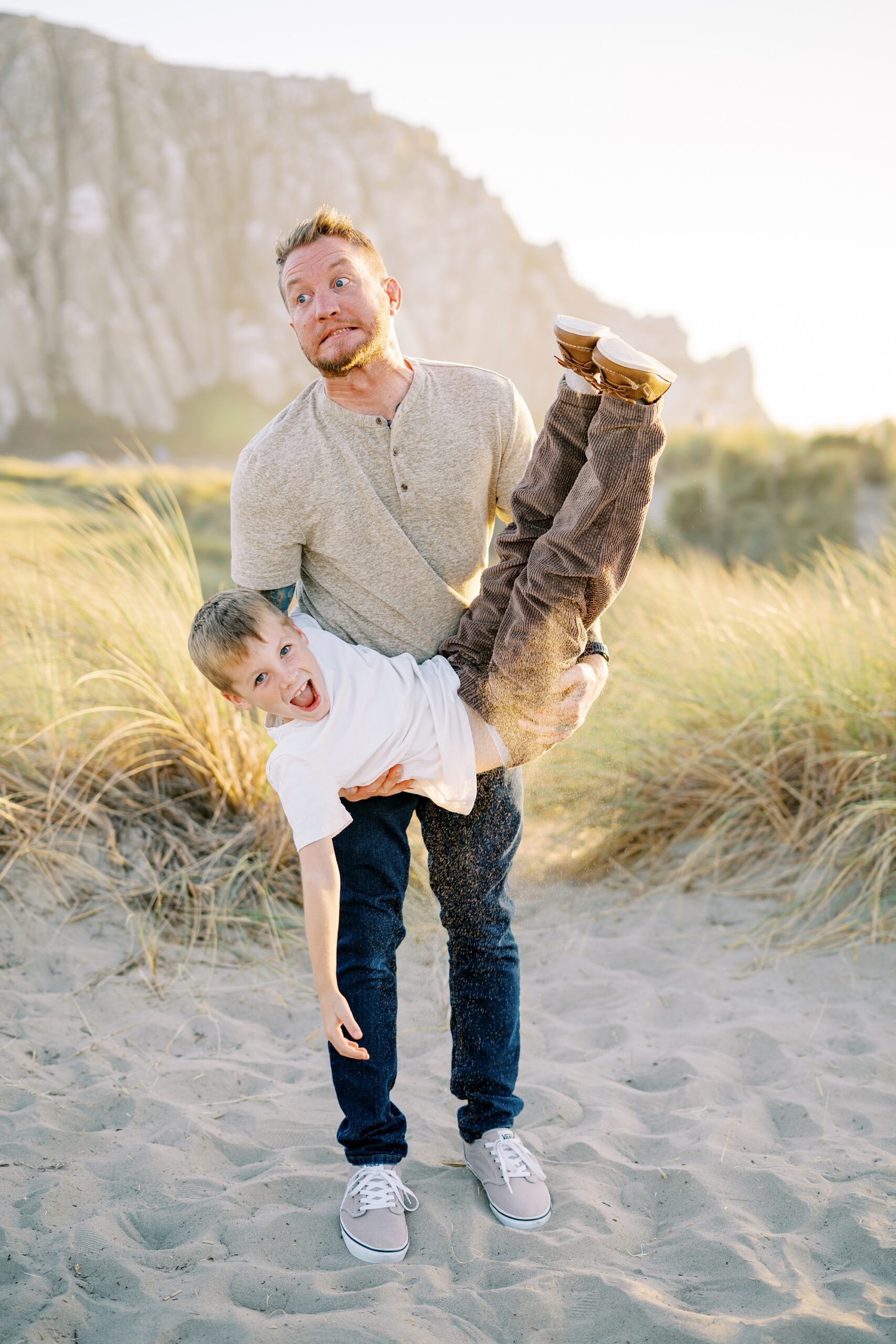 Dad and eight year old being silly in the sand in front of morro rock by Morro Bay Family Photographer Austyn Elizabeth Photography
