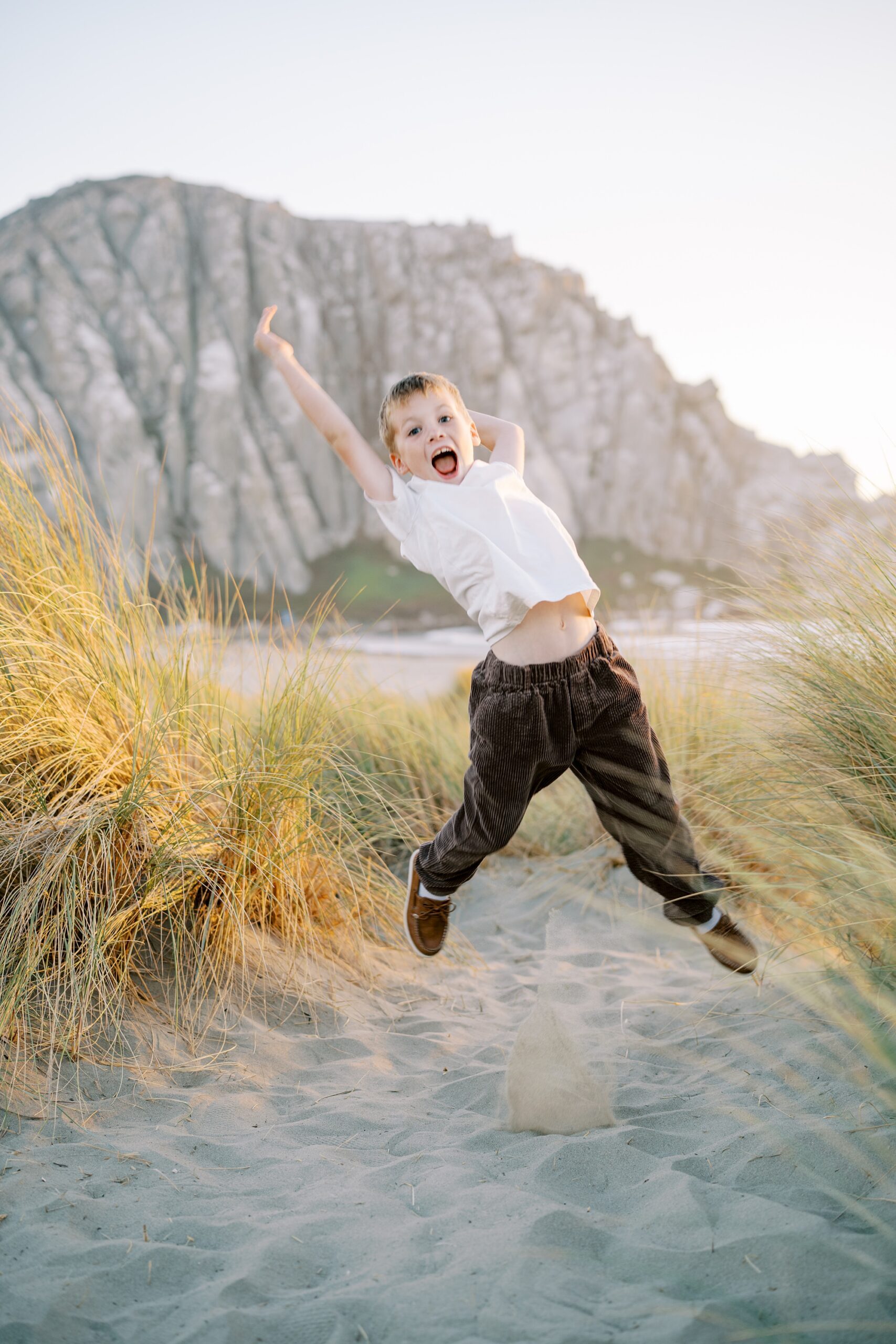 eight year old portraits while jumping in front of morro rock during golden hour by Morro Bay Family Photographer Austyn Elizabeth Photography